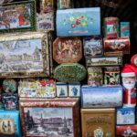 Vecchie scatole di latta pubblicitarie vintage, colorate e decorate, esposte su uno sfondo neutro.